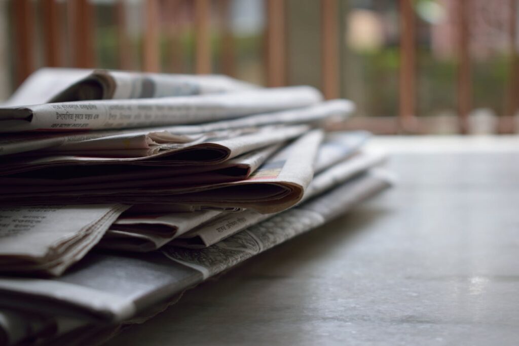 pexels photo 518543 A close-up of a stack of newspapers resting on a desk, symbolizing information and media.