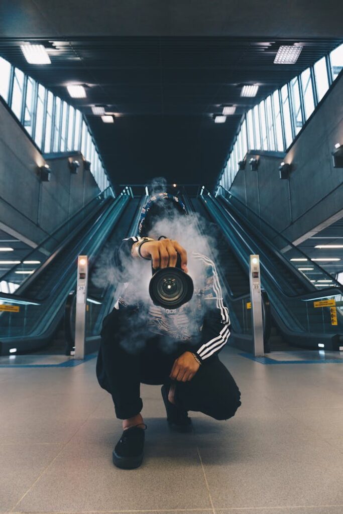 pexels photo 598917 Person holding a camera in a smoke-filled urban setting with escalators.